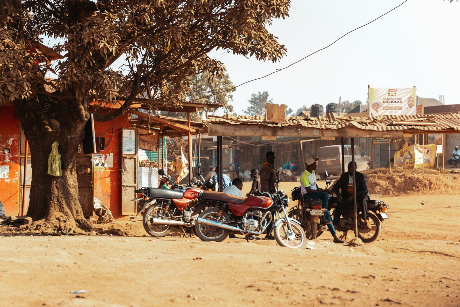 Motorbikes parked under a tree in a Ugandan village, capturing local lifestyle and community.